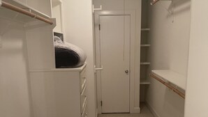 Un pasillo estrecho con un armario a la izquierda, una puerta al final y una estantería a la derecha.