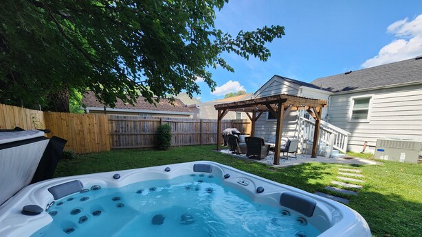 Un jardin avec un jacuzzi, une pergola en bois et un espace clos aménagé avec du mobilier d’extérieur.