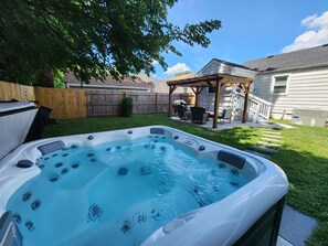 Patio trasero con jacuzzi, un pérgola de madera y un área cercada con mobiliario exterior.