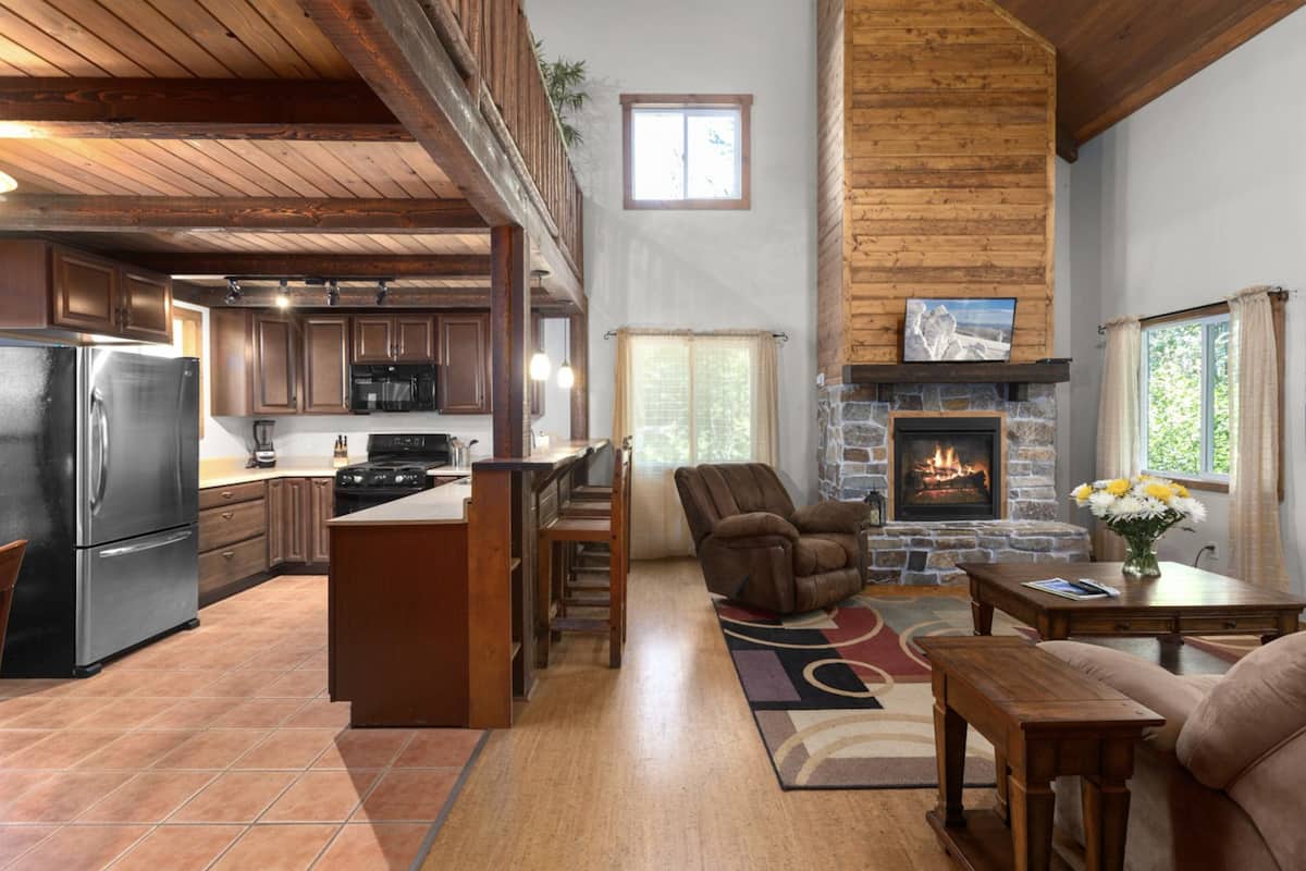 A spacious kitchen with a central island, a stone fireplace, and a cozy seating area with a sofa and armchair.