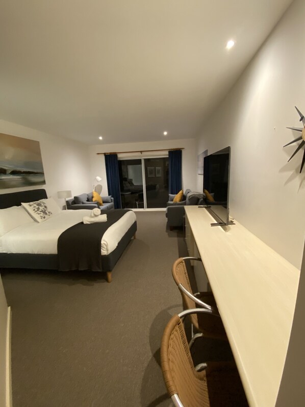 A hotel room with a bed, a desk, a chair, a TV, and a balcony with a view.