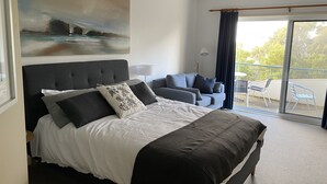 Ein modernes Schlafzimmer mit einem großen Bett, einem Sofa, einem Balkon mit Stühlen und einem Bild an der Wand.
