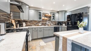 A modern kitchen with grey cabinets, a black refrigerator, and a stone backsplash. - Desert Ruby: Stargaze, Spacious, Hot Tub, Fire pit, Fenced, Pet Friendly (Yucca Valley)