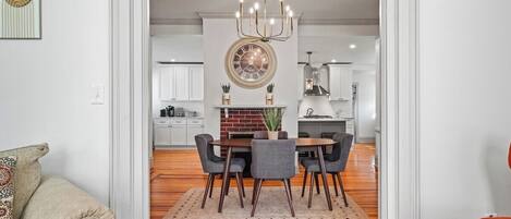 A modern kitchen with a round clock, wooden flooring, and a dining area with a table and chairs.