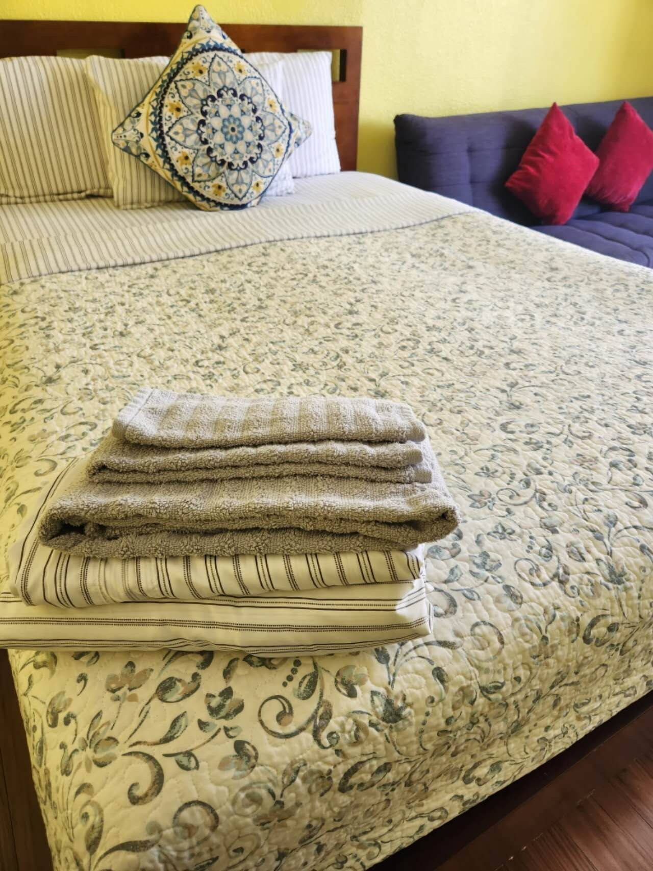 Un letto con una coperta a motivi floreali, una pila di asciugamani piegati e un cuscino decorativo.