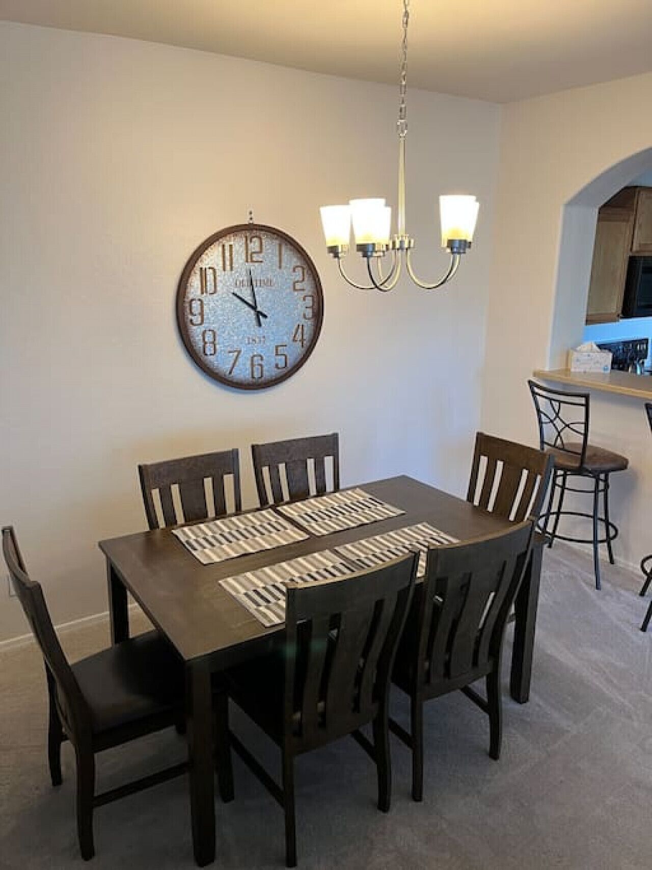 A dining area with a wooden table and chairs, a wall clock, and a chandelier.