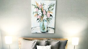 A bedroom with a bed, two bedside lamps, a headboard, and a wall-mounted painting.
