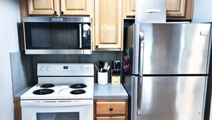 A kitchen with a microwave, stove, refrigerator, and wooden cabinets.
