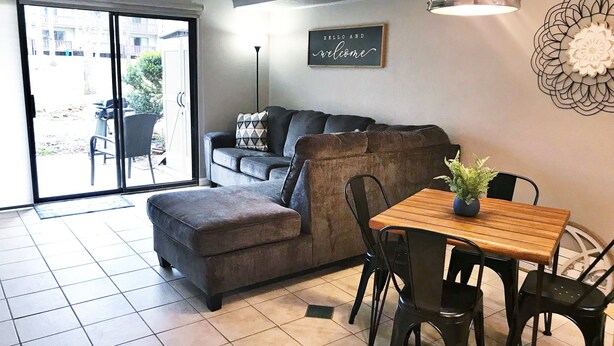 A living room with a sofa, a dining table with chairs, a potted plant, and a wall-mounted sign.