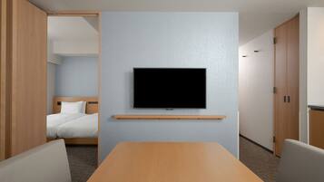 Une chambre d’hôtel équipée d’un téléviseur à écran plat fixé au mur, d’une table en bois et de deux chaises.