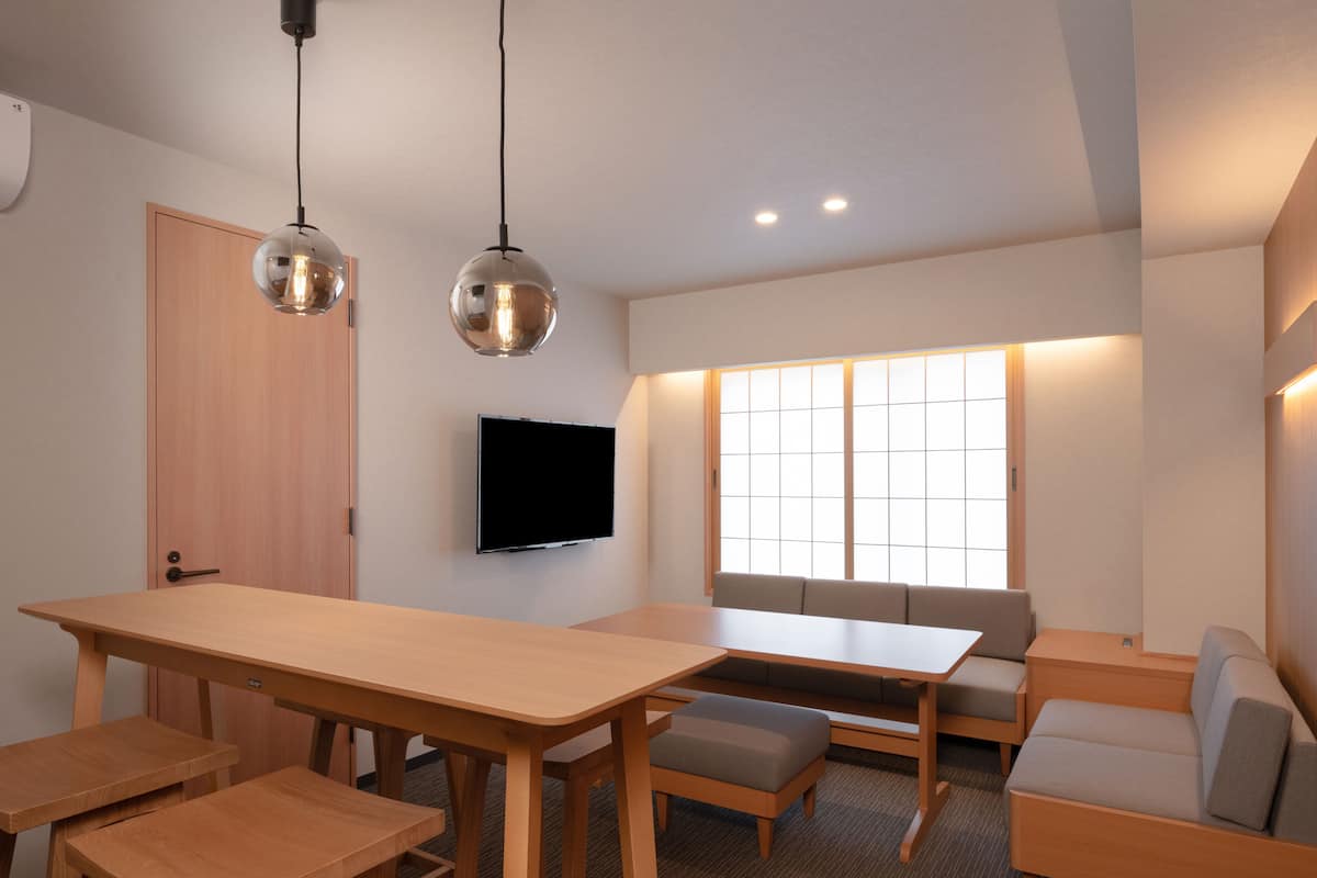 A modern room with a wooden table, benches, a sofa, and a TV mounted on the wall.