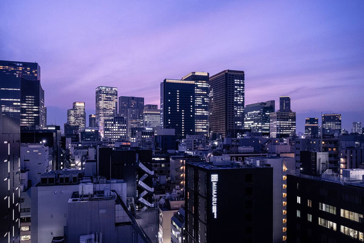 A city skyline at dusk with illuminated buildings and a mix of high-rise and mid-rise structures.