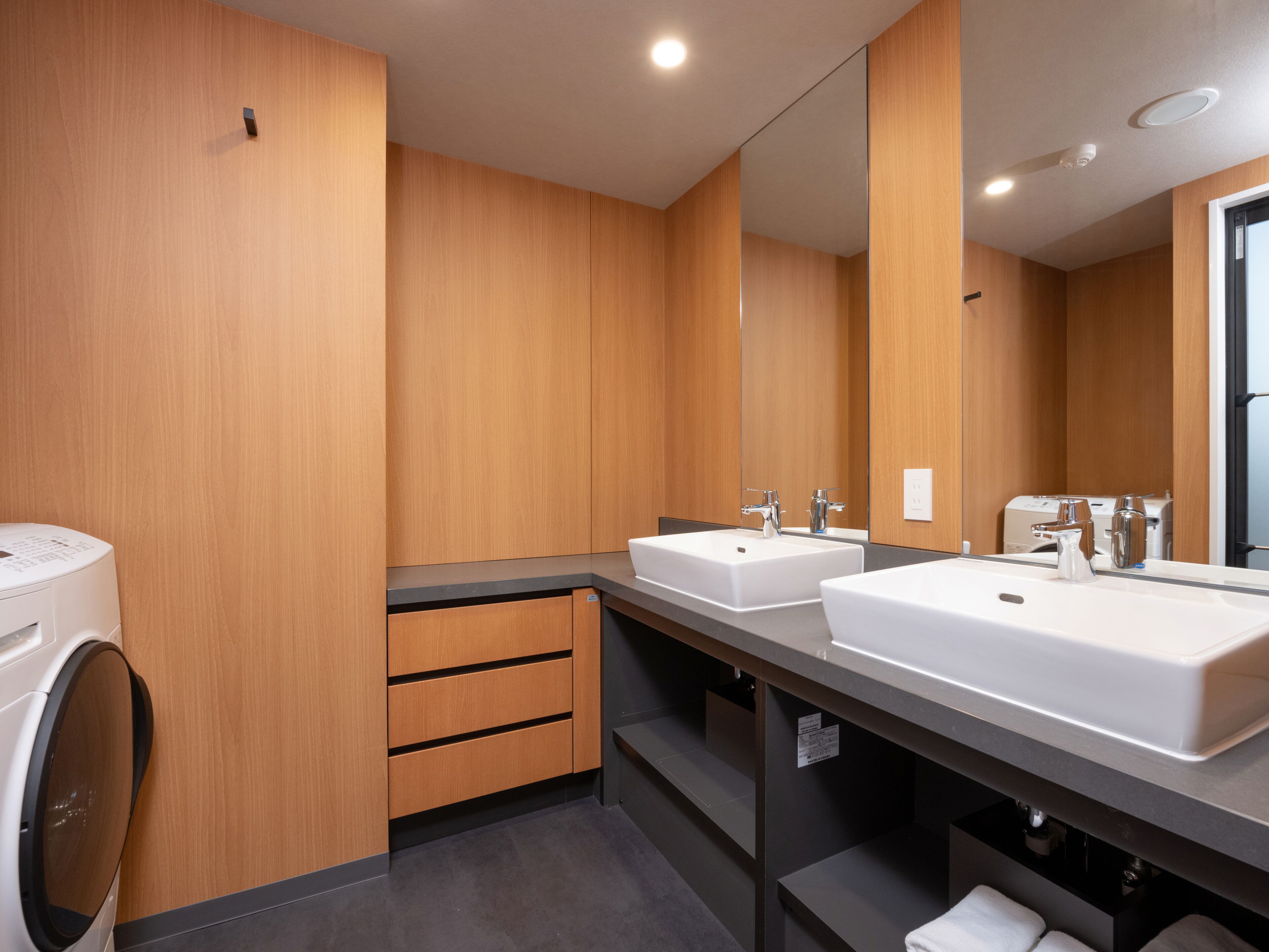 A modern bathroom with two sinks, wooden paneling, a mirror, and a washing machine.