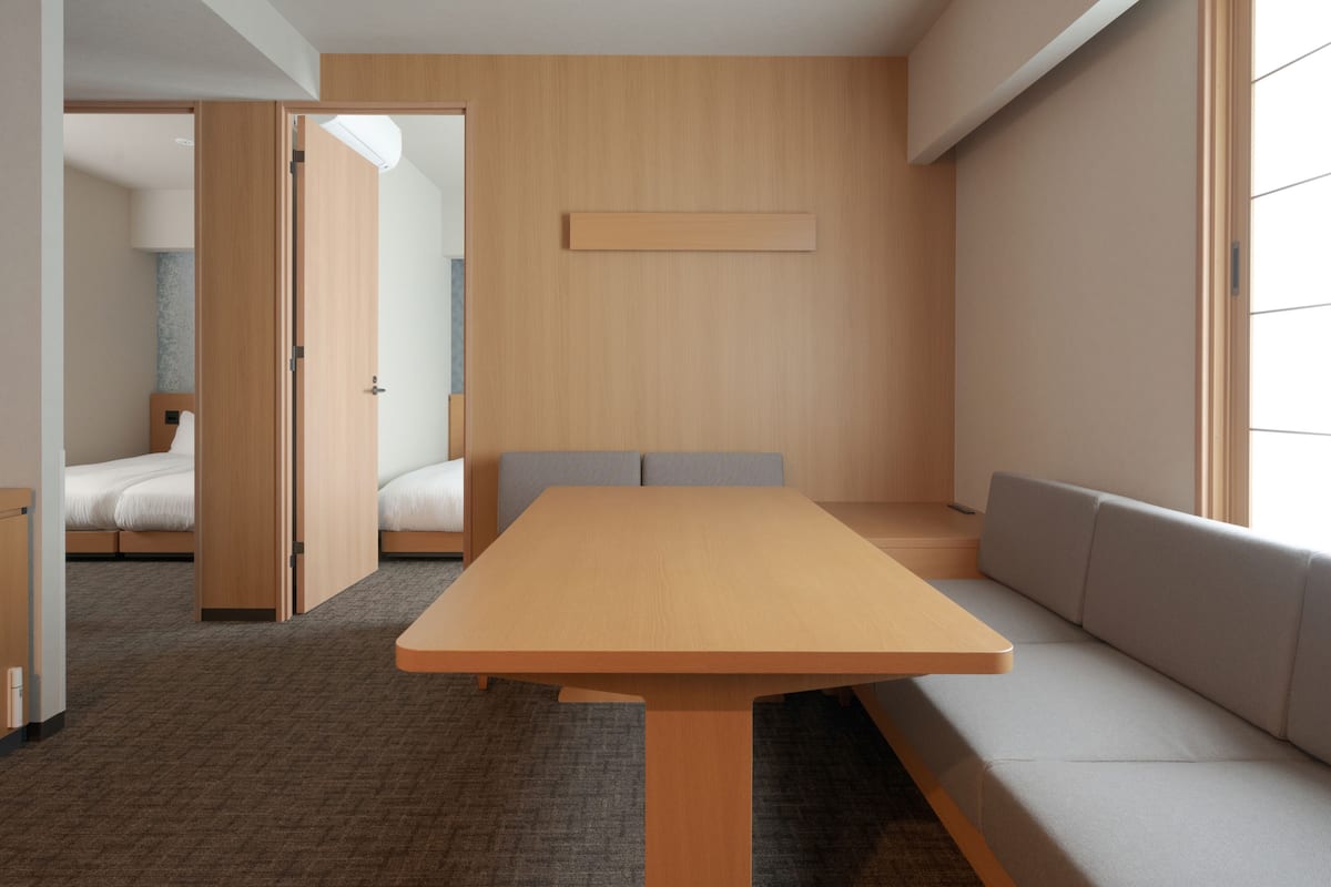 A modern hotel room with a wooden table, a sofa, a bed, and a large window.