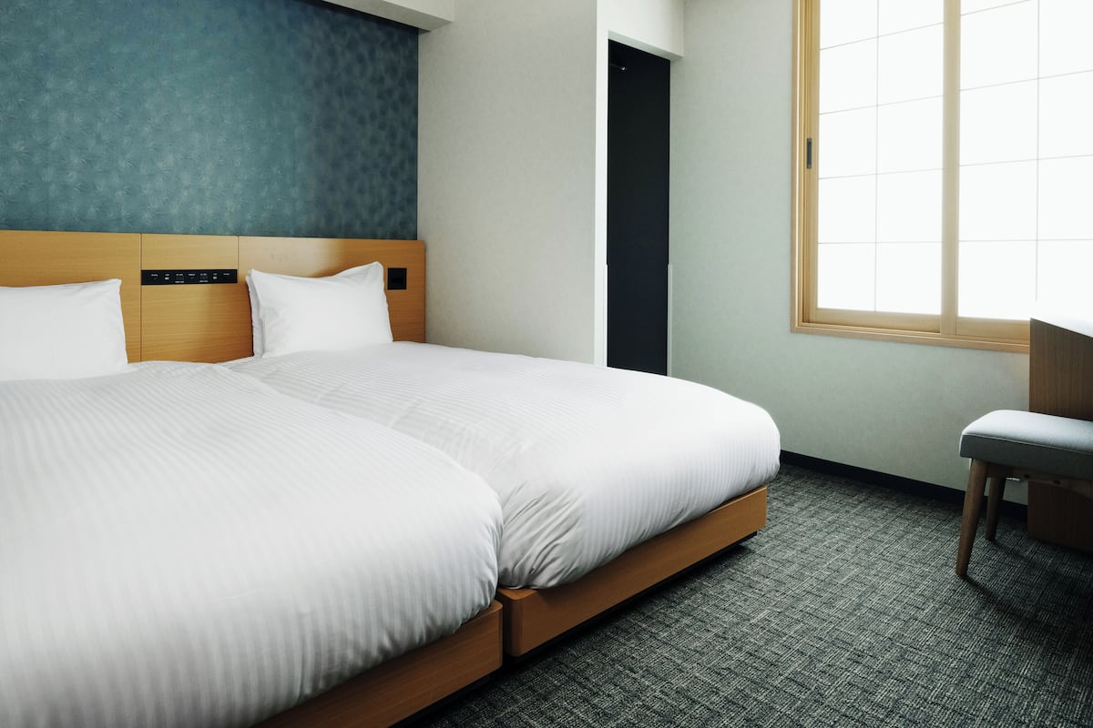 A modern hotel room with a large bed, a desk, and a window with blinds.