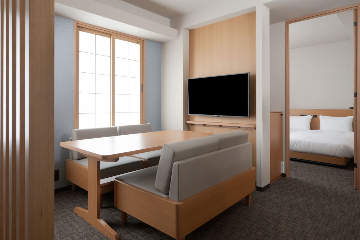 A modern hotel room with a wooden desk, a sofa, a flat-screen TV, and a bed.