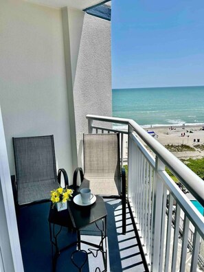 Un balcon avec une table, des chaises et une vue sur la plage.
