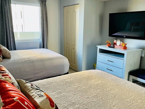 Une chambre d’hôtel avec deux lits, une télévision, une commode et une fenêtre avec des rideaux.