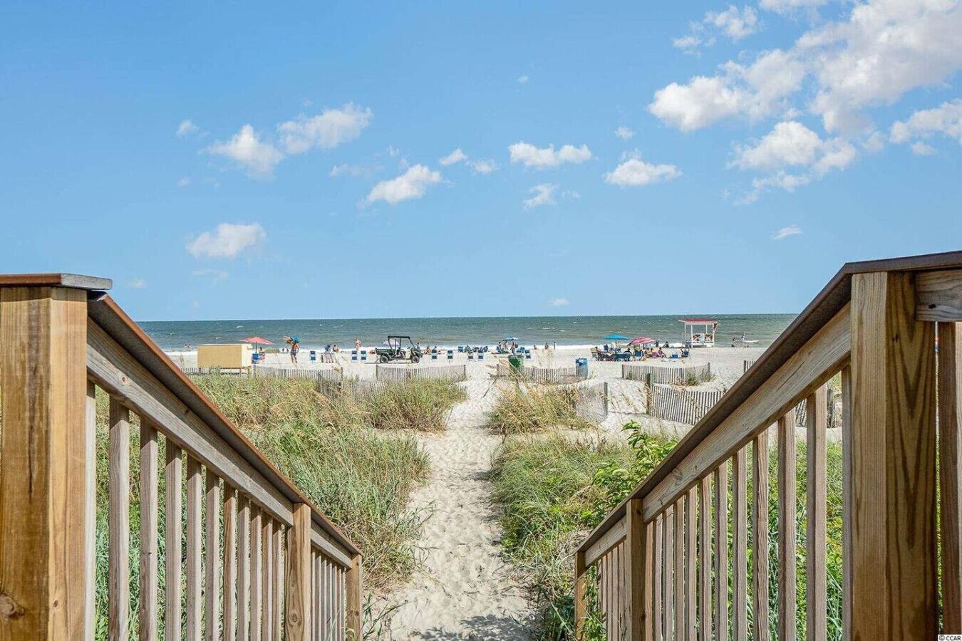 A wooden staircase leading to a beach with people and beach umbrellas.