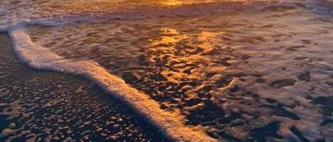 A beach at sunset with waves gently lapping the shore.