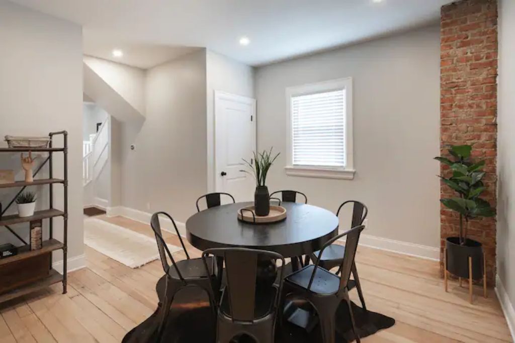 A dining area with a round table, six chairs, and a potted plant.