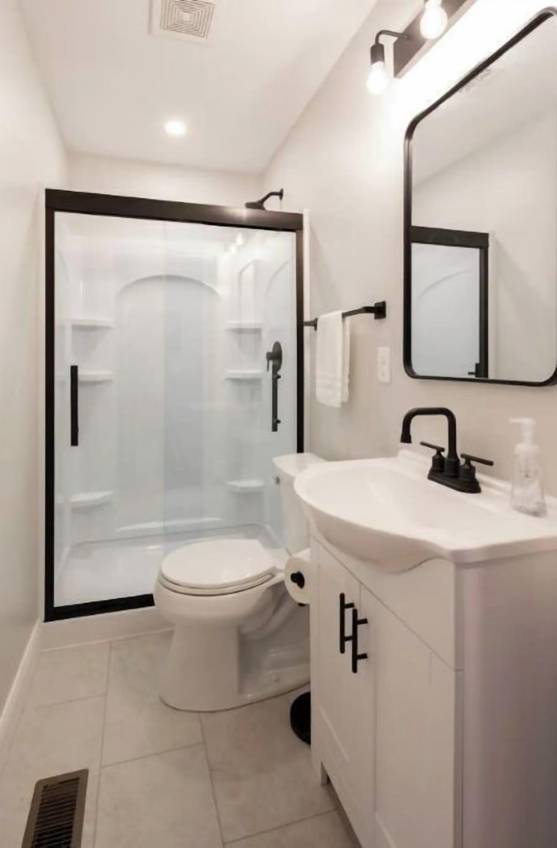 A modern bathroom with a glass-enclosed shower, a white sink with a black faucet, and a mirror above the sink.
