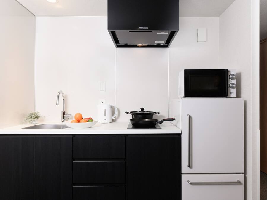 Una cocina moderna con campana extractora negra, microondas, refrigerador blanco y un lavamanos con hervidor y naranjas en la encimera.
