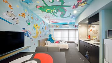 A room with a large TV, a sofa, a dining area with a kitchen, and a ceiling with colorful wall art.