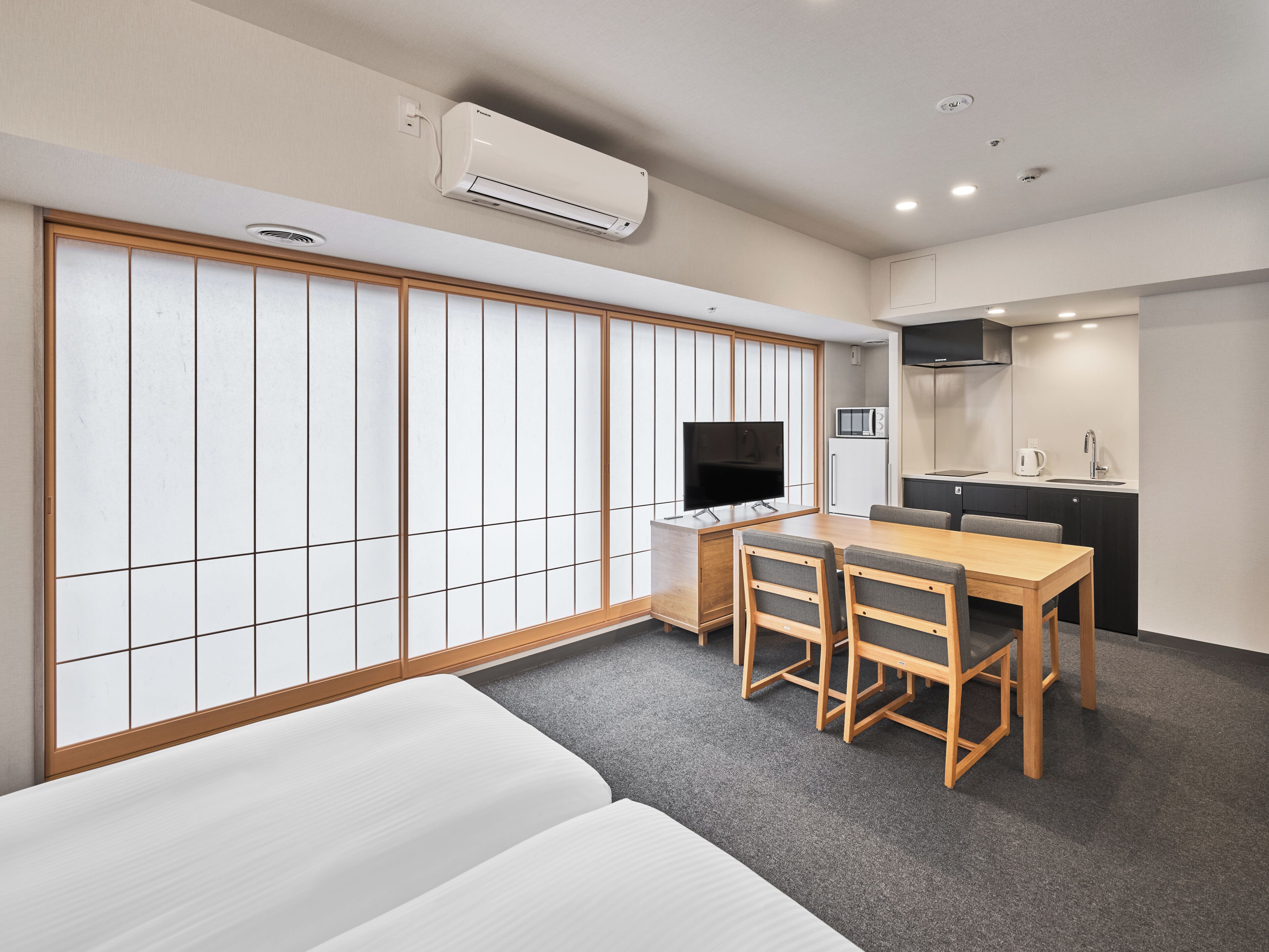 Une chambre d’hôtel moderne équipée d’un lit, d’une table à manger avec des chaises, d’un téléviseur, d’un coin cuisine et d’un appareil de climatisation.