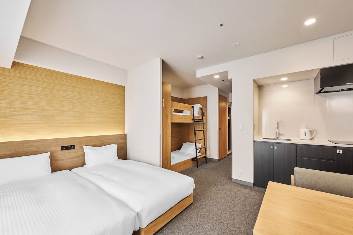 A hotel room with two beds, a kitchenette, and a small dining area.