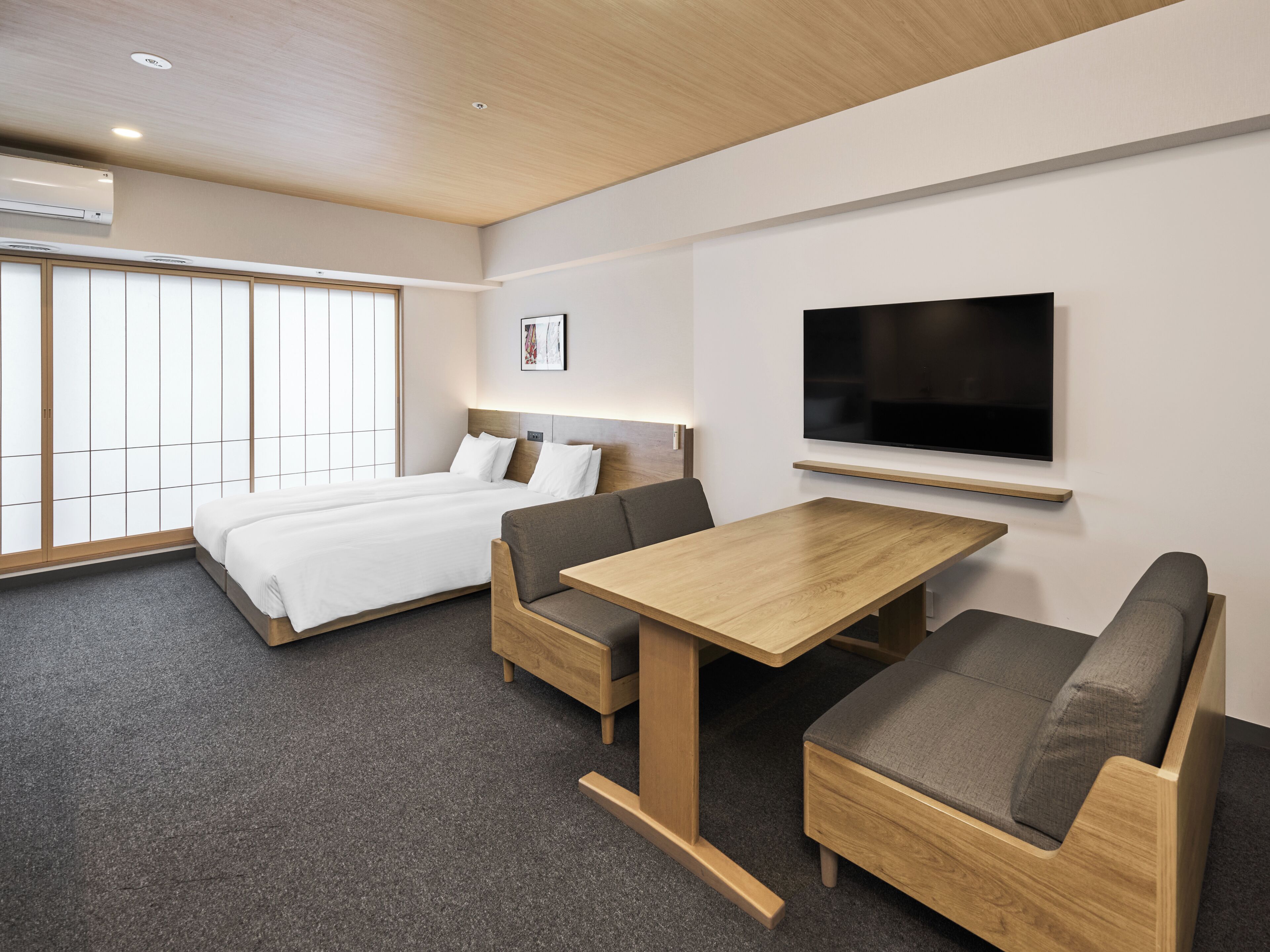 A modern hotel room with a bed, a TV mounted on the wall, and a small wooden table.