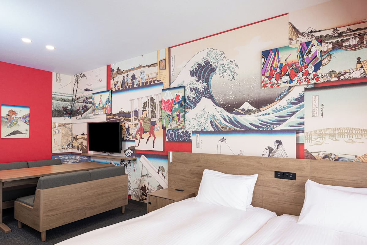 A hotel room with a bed, a TV, and a wall decorated with Japanese art.
