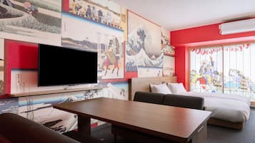 Quarto de hotel moderno com uma televisão grande, uma cama, um sofá e uma mesa de jantar. As paredes são decoradas com arte japonesa tradicional.