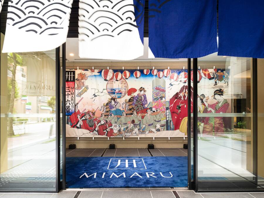 A hotel entrance with a traditional Japanese mural, a blue carpet with the hotel's name, and a modern glass door.