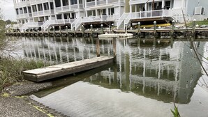 A waterfront property with a dock extending into a calm body of water, surrounded by grassy areas and a building with multiple decks and railings. - Family fun! Beach, Kayaking, yard games, large fenced yard, fire pit. 2 mi beach (Ocean View)