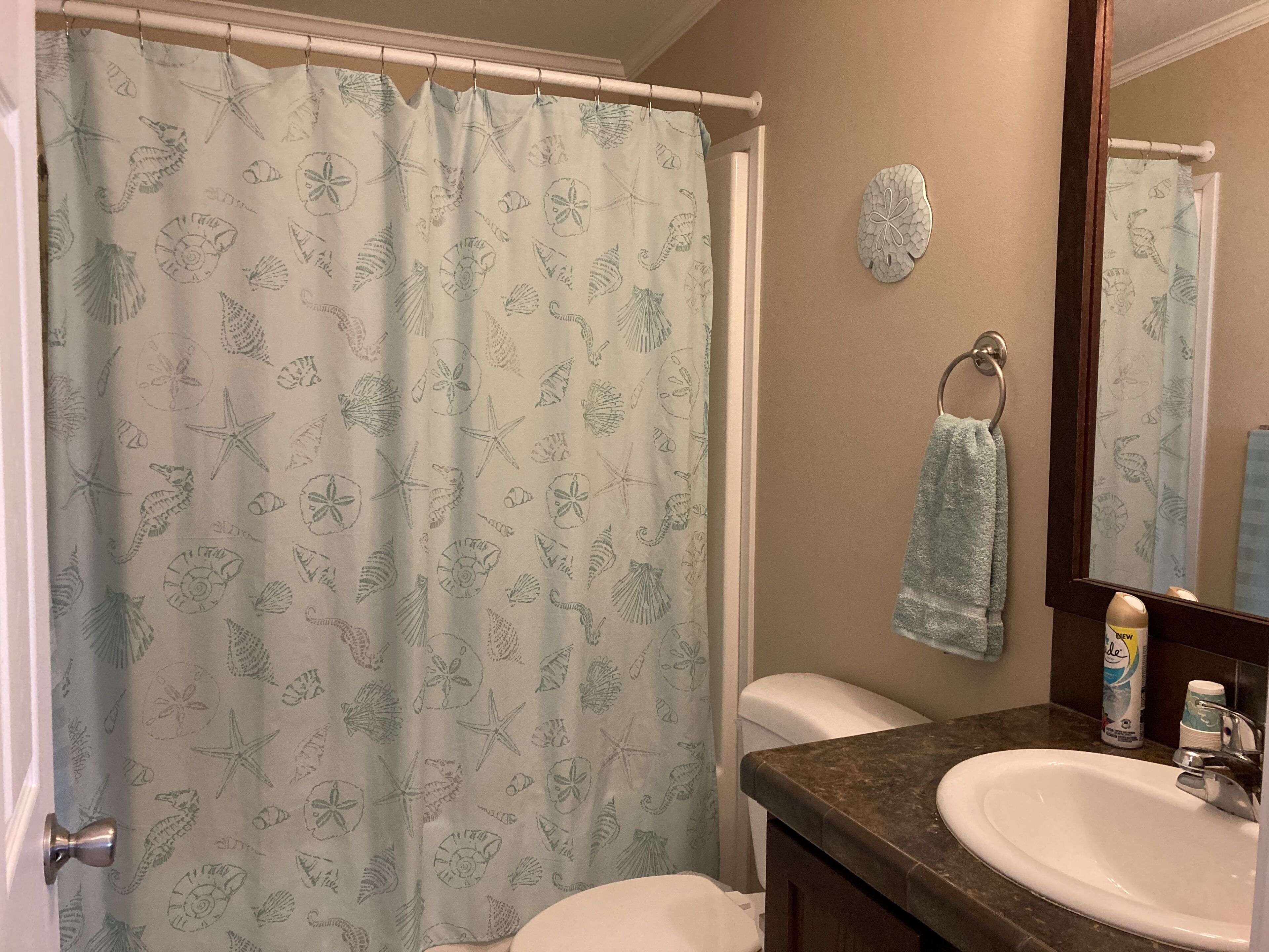 Une salle de bain avec un rideau de douche orné d’un motif représentant la vie marine, des toilettes blanches, un lavabo avec une serviette et un miroir.