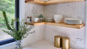A kitchen with wooden shelves holding plates, glasses, and books. There is a window with greenery outside. - Family Style Cottage 5 minutes from the Gaslight District  (North dumfries)