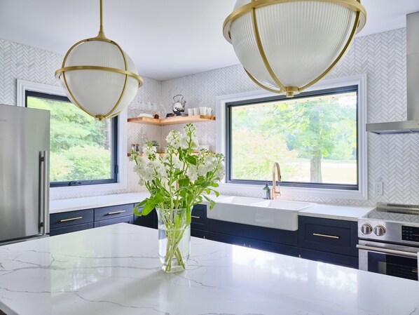 Una cocina moderna con encimera de mármol, electrodomésticos de acero inoxidable y un amplio ventanal con vistas a zonas verdes.