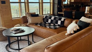 Una sala de estar acogedora con un sofá de cuero, una mesa redonda y vistas al exterior a través de grandes ventanales.