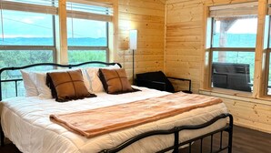 Un dormitorio tipo cabaña de madera con cama, ventilador de techo y ventanas amplias.