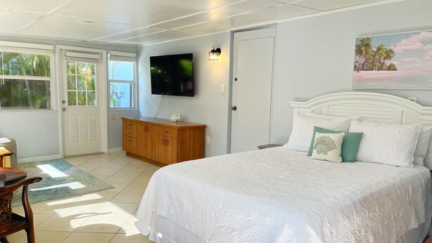 A bedroom with a large bed, a TV mounted on the wall, a wooden dresser, and a door leading to a balcony. - Sarasota Gateway Beach House (Sarasota)