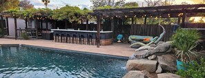 Zona de piscina amb bar, seients i una pèrgola amb llums enfilades.