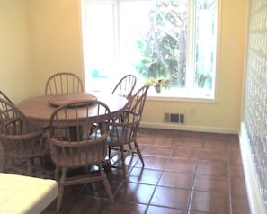 A dining area with a round wooden table and chairs, a window with a view of greenery, and a tiled floor. - Private bedroom and parking near downtown Baltimore  (Bethesda)