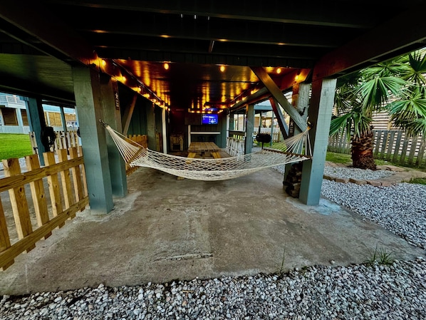 Relax in a serene outdoor space with a hammock suspended between two pillars, surrounded by lush greenery and a palm tree.
