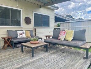 An outdoor patio with a grey sofa, a wooden coffee table, and a potted plant.