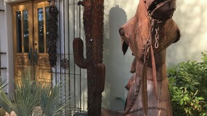 A rustic outdoor area with a metal gate, a cactus sculpture, and a potted plant with white flowers. - Walk to Old Town, Heated Pool, Fast Internet,  Continental Breakfast included.  (Scottsdale)