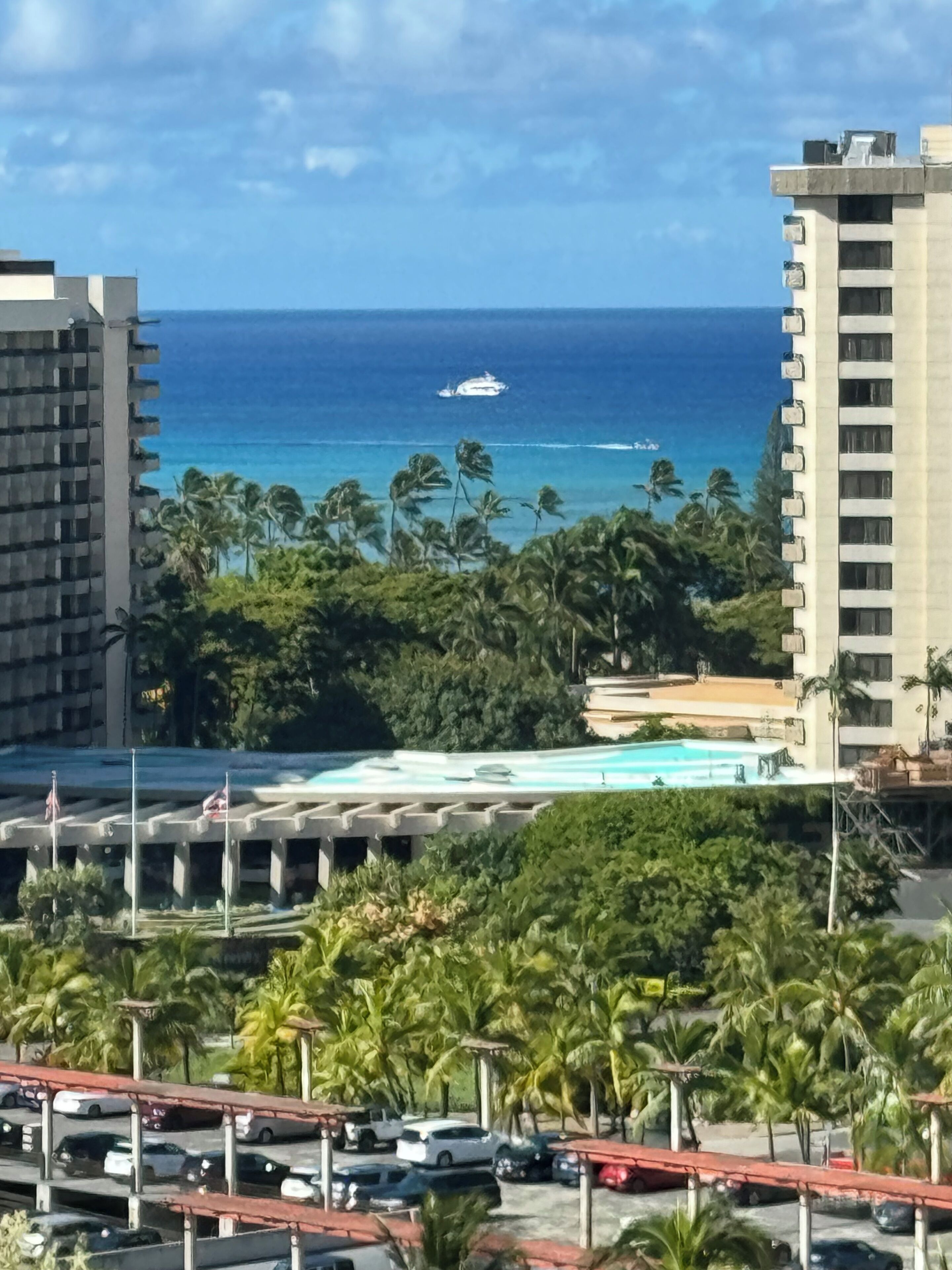 A coastal view with a swimming pool, palm trees, and a distant yacht.