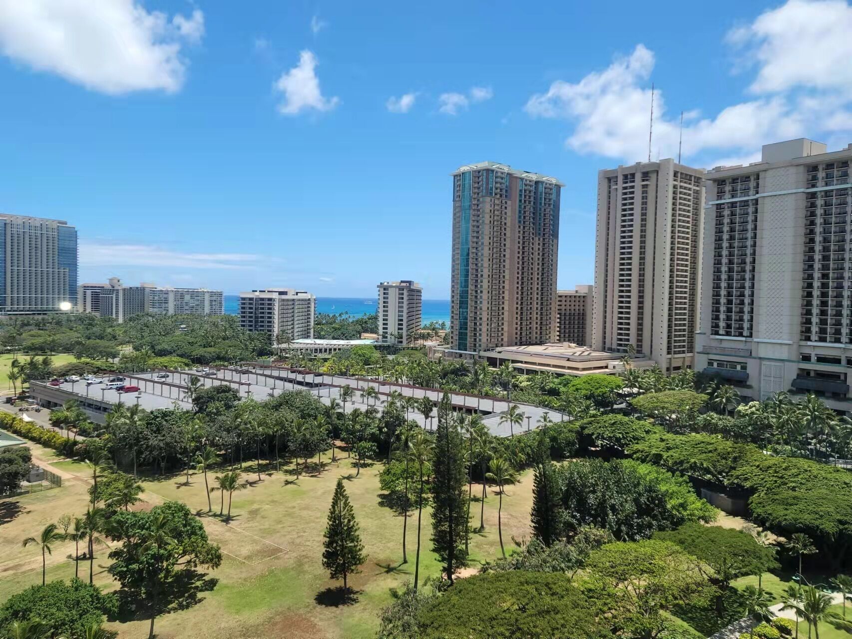 A high-rise residential area with multiple apartment buildings, a parking lot, and a well-maintained park with trees and grass.
