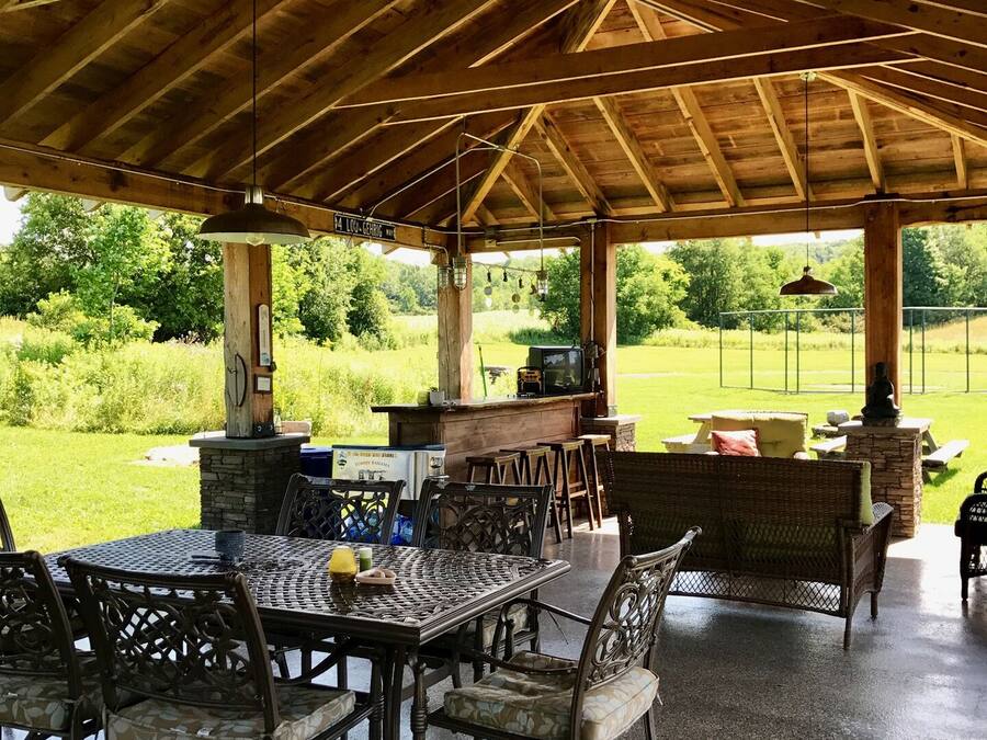 An outdoor covered patio with a stone fireplace, metal table and chairs, and a stone bench.