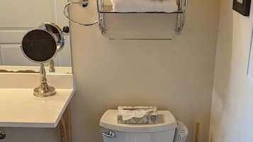 A bathroom with a toilet, a sink with a mirror, a towel rack with towels, and a toilet paper holder.